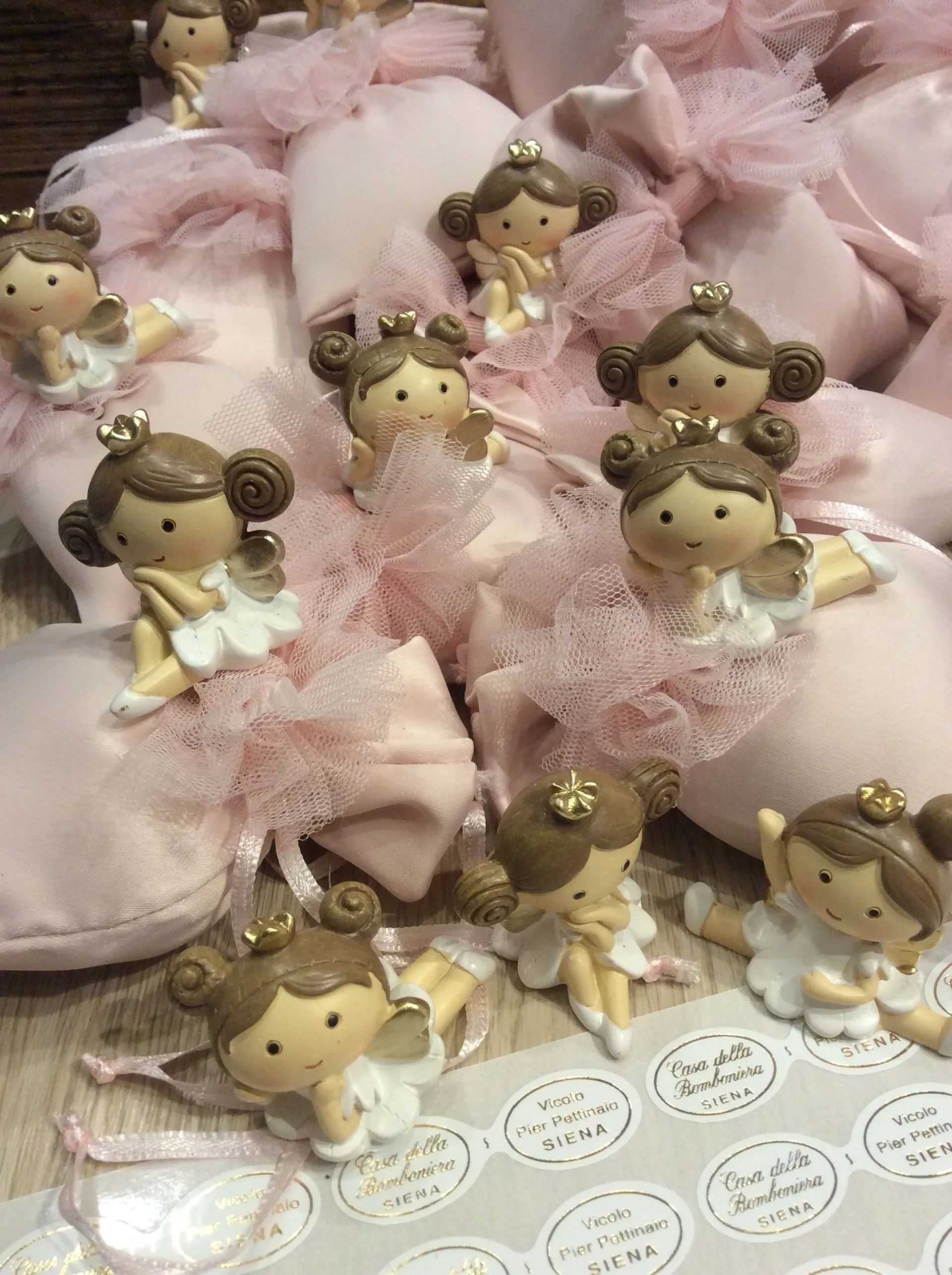 Bomboniere rosa per baby shower con minuscole statuine di angioletti disposte tra fiocchi di tulle e raso