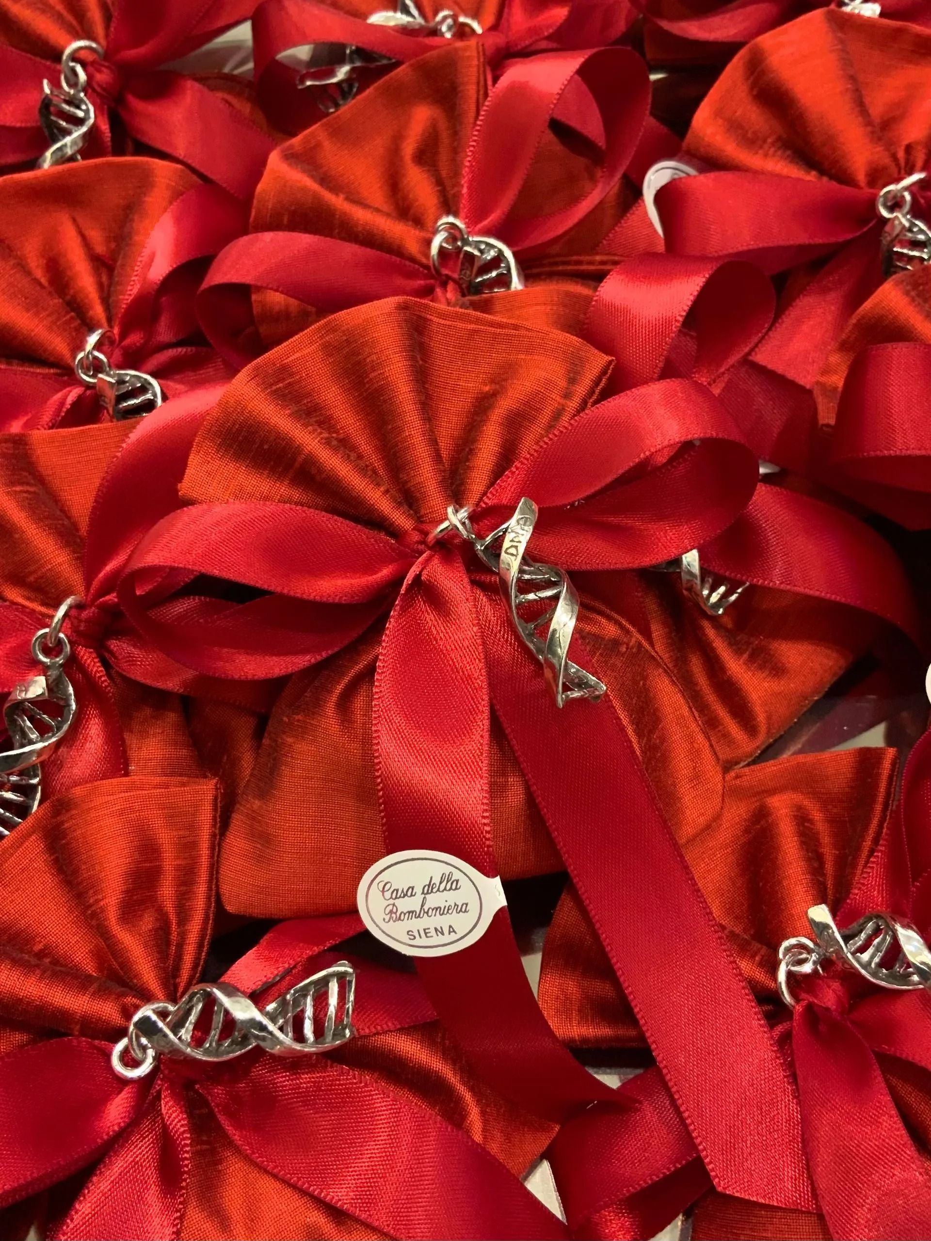 Fiocchi regalo in raso rosso con nastri argentati e una piccola etichetta rotonda, disposti in una pila festiva.