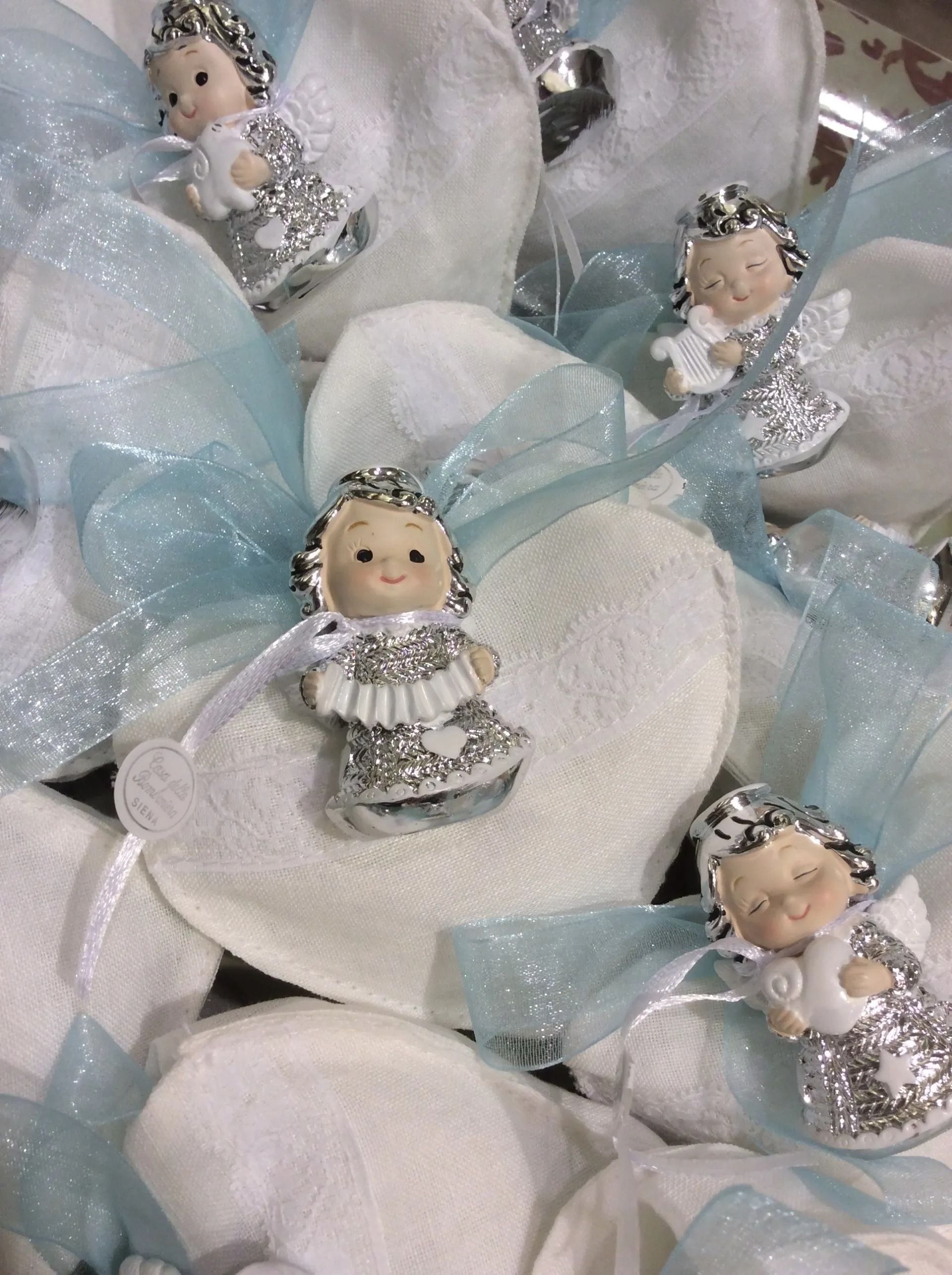Piccole bambole angelo in abiti argentati su petali bianchi simili a fiori con nastri di tulle azzurro pallido.