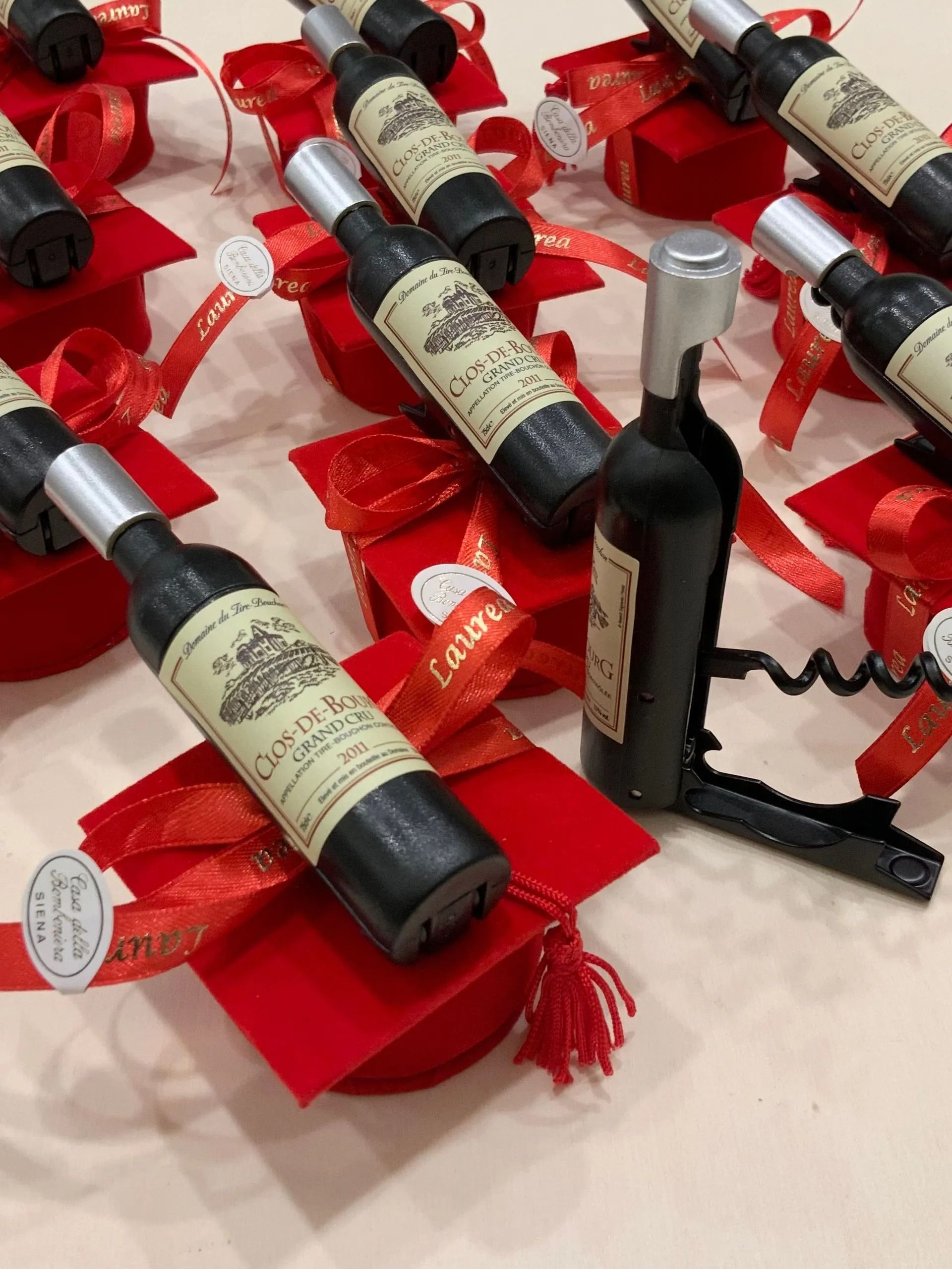 Bottiglie di vino esposte su supporti di stoffa rossa con fiocchi di nastro su una tavola apparecchiata per le feste.