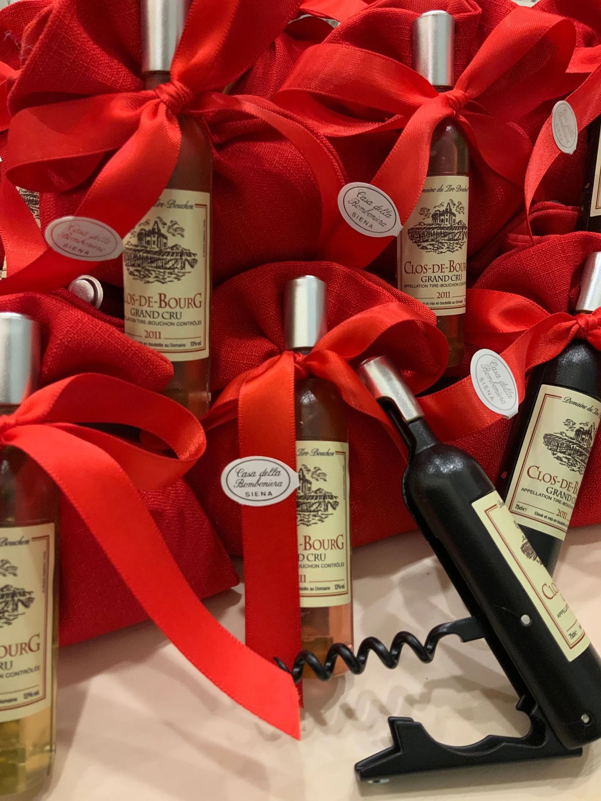 Cesti regalo rossi con bottiglie di vino, ciascuno avvolto in un nastro rosso e decorato con fiocchi bianchi.
