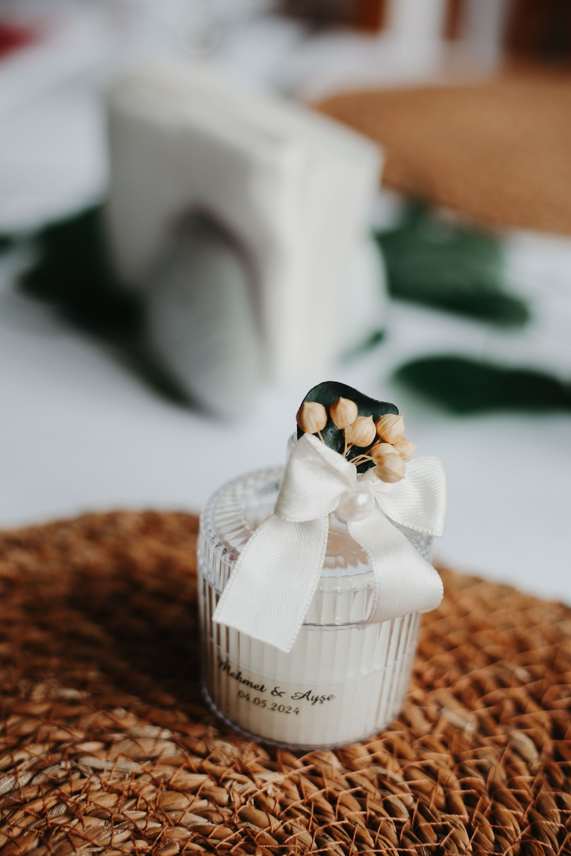 Piccolo vasetto regalo bianco con nastro e fiori secchi su una tovaglietta intrecciata.