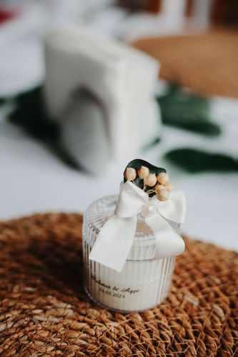 Piccolo vasetto regalo bianco con nastro e fiori secchi su una tovaglietta intrecciata.