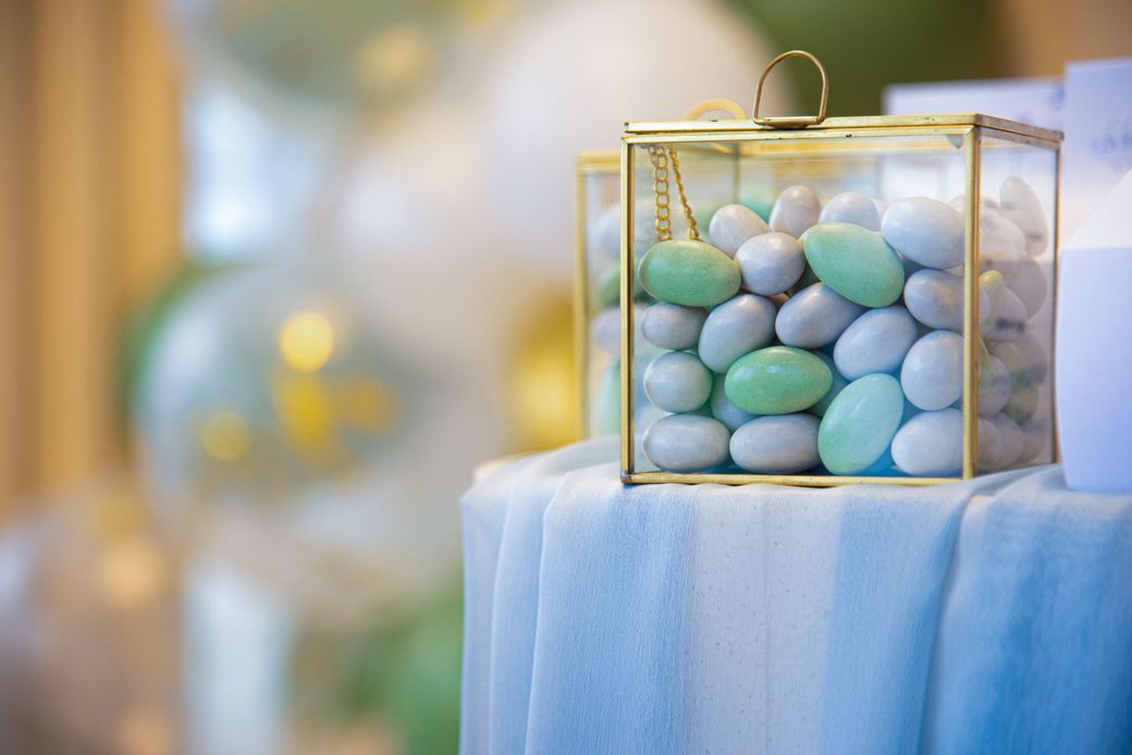Uova di cioccolato color pastello in una scatola trasparente su una tovaglia blu, con uno sfondo di festa pastello sfocato.