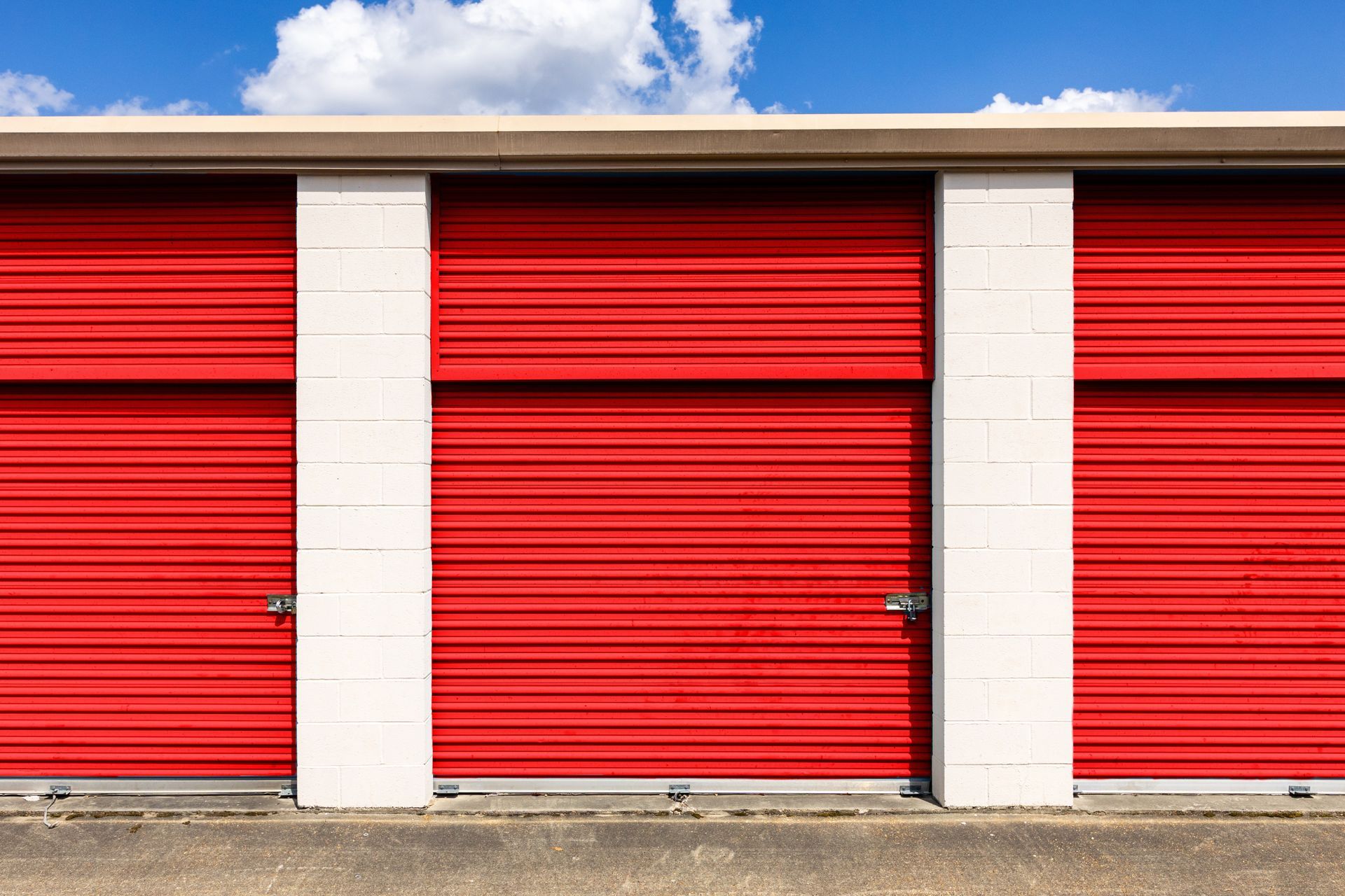 Row of red self-storage unit doors at a storage facility under a clear blue sky Row of red self-storage unit doors at a storage facility under a clear blue sky