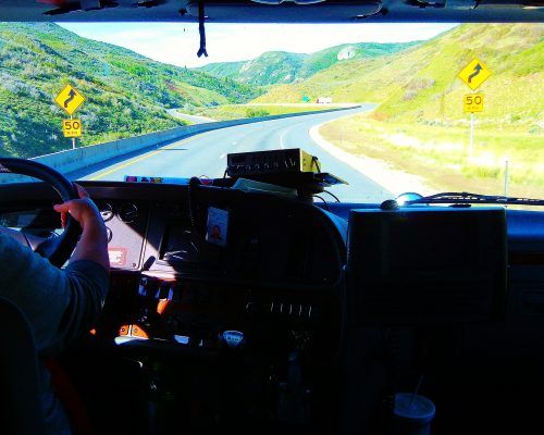 A person is driving a truck down a highway with mountains in the background.