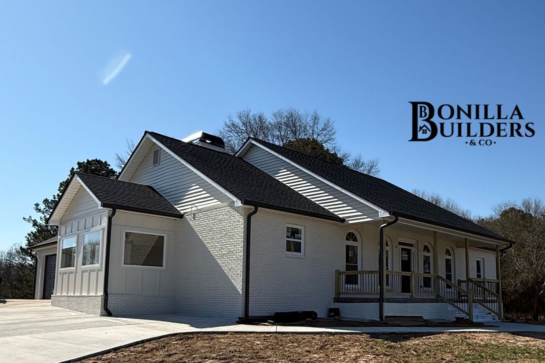 White house with dark roof on a clear day, branded Bonilla Builders logo in the corner