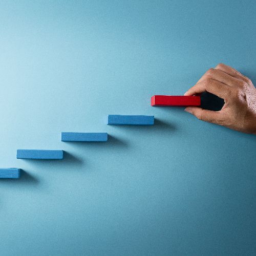 A hand places a red rectangular block onto a stack of blue blocks arranged like a staircase against a blue background.