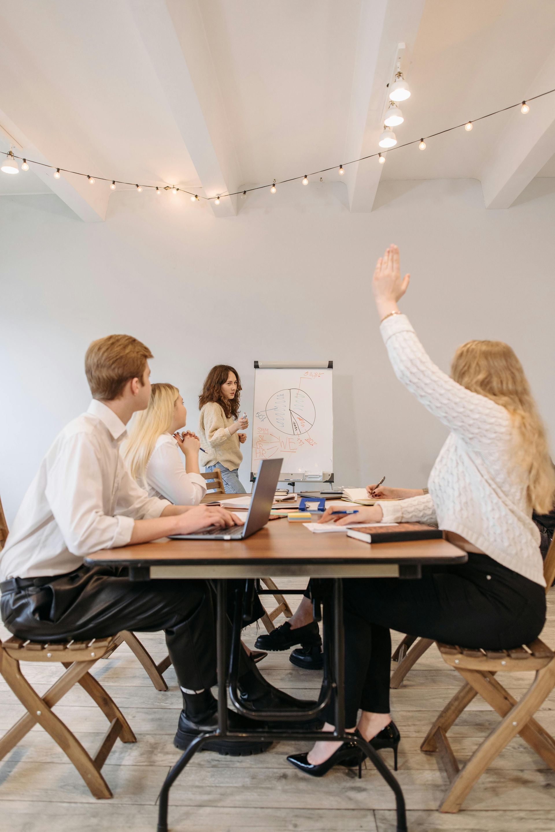 A group of people sitting at a table with one person raising their hand during a presentation in an office setting.
