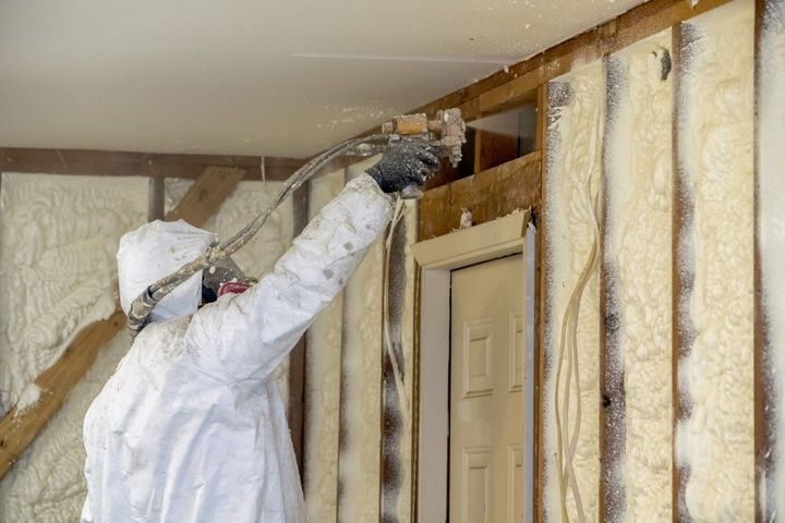 Technician applying spray foam insulation inside framed wall cavity