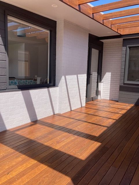 Wooden deck with sunlight and shadows, next to white and brick walls, dark framed windows - Brad Griffiths Building In Culburra Beach, NSW