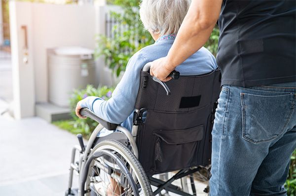 A caregiver pushes a person in a wheelchair outdoors.