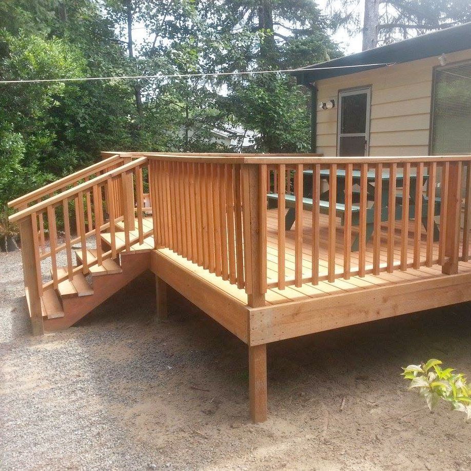Wooden deck and ramp attached to a house, with a railing and gravel yard below.