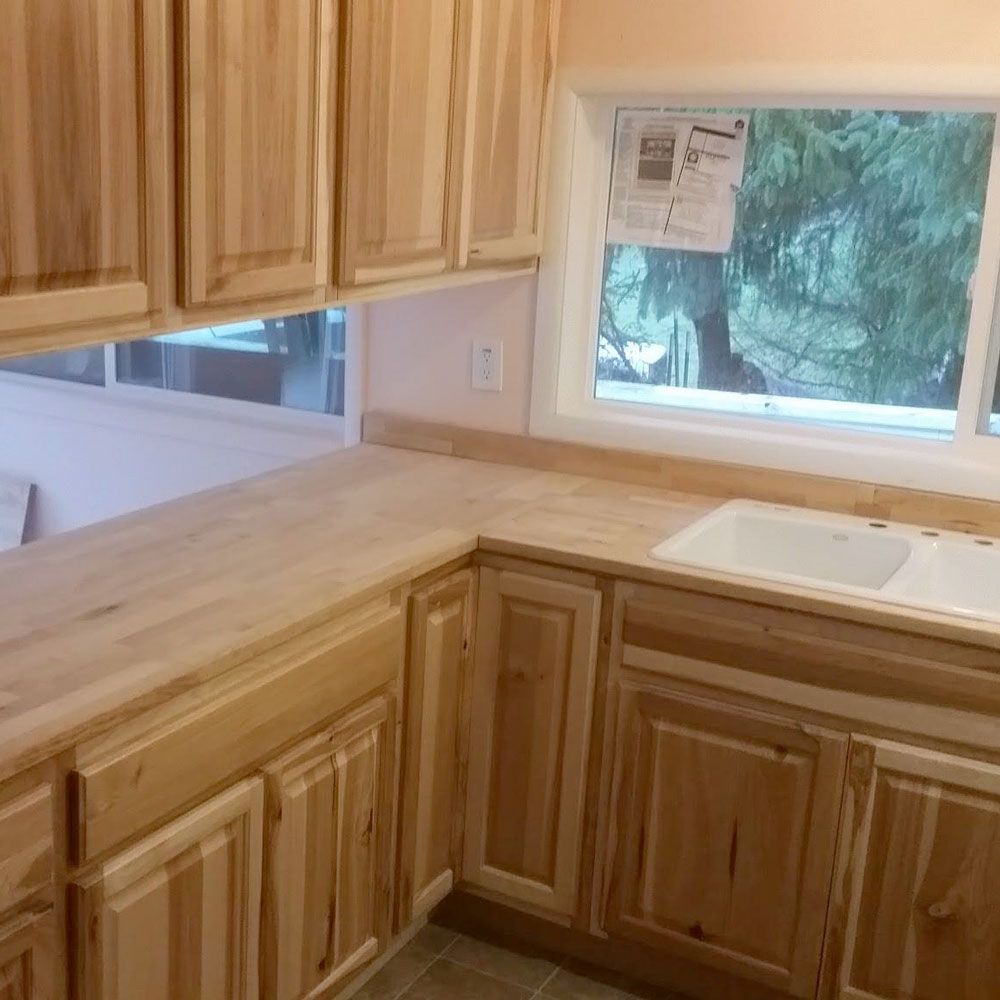 Wooden kitchen corner with light cabinets, tan countertops, and windows above the sink.
