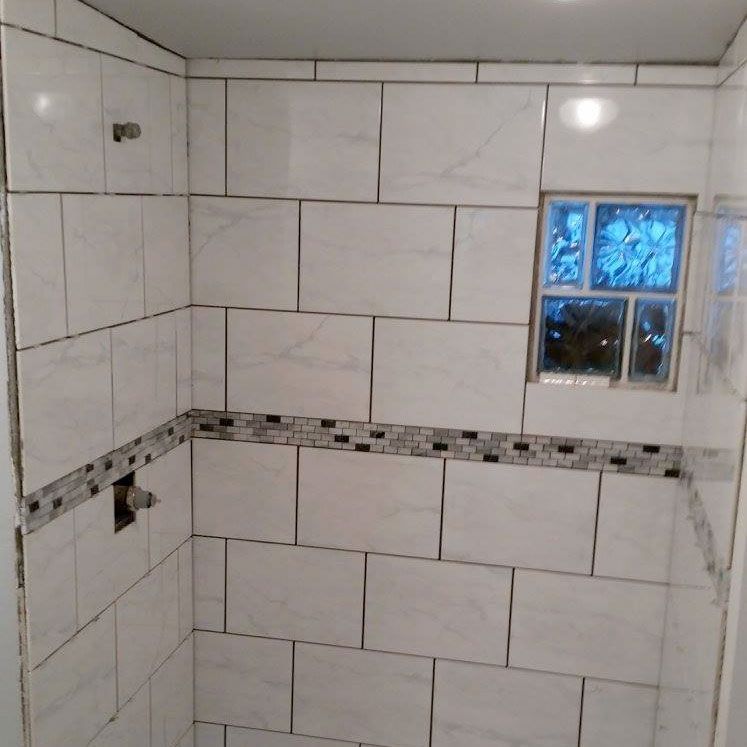 Tiled bathroom shower stall with white tiles, mosaic accent band, and a small glass block window.