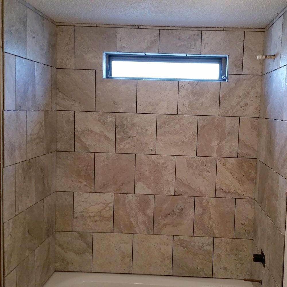 Empty tiled shower with a small frosted window near the top.