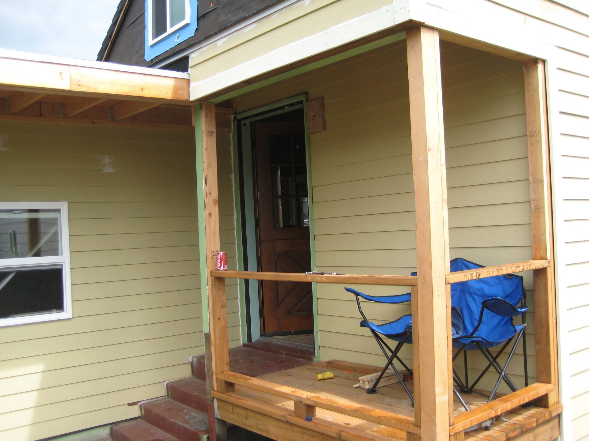 Front porch of a house with a wooden bench, blue folding chair, and open front door