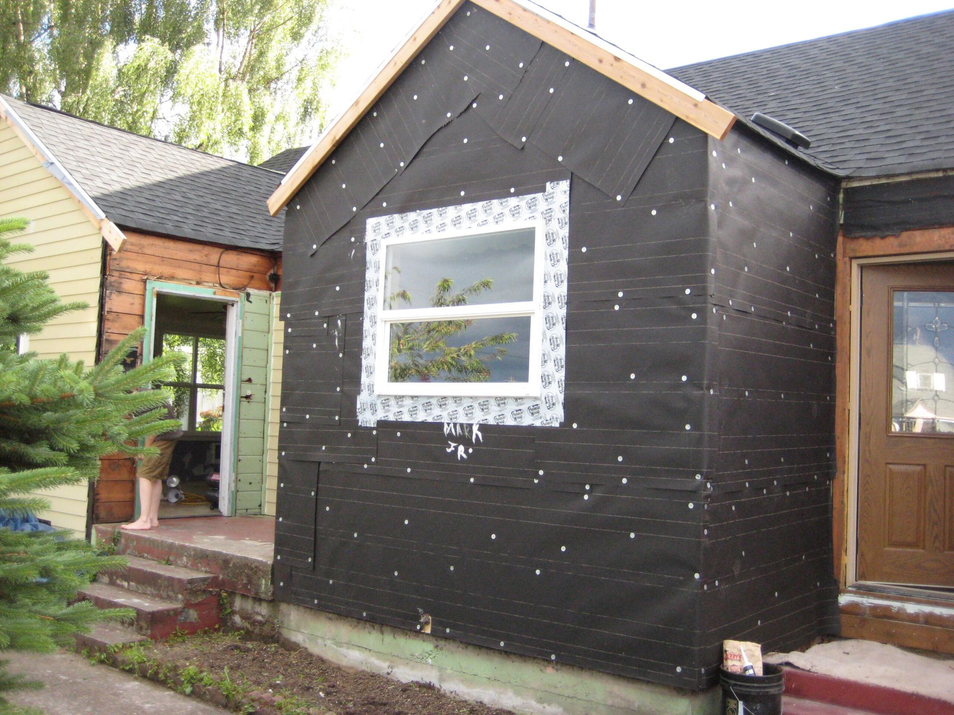 Black-clad house extension with white-trimmed window beside a brick home and wooden door.