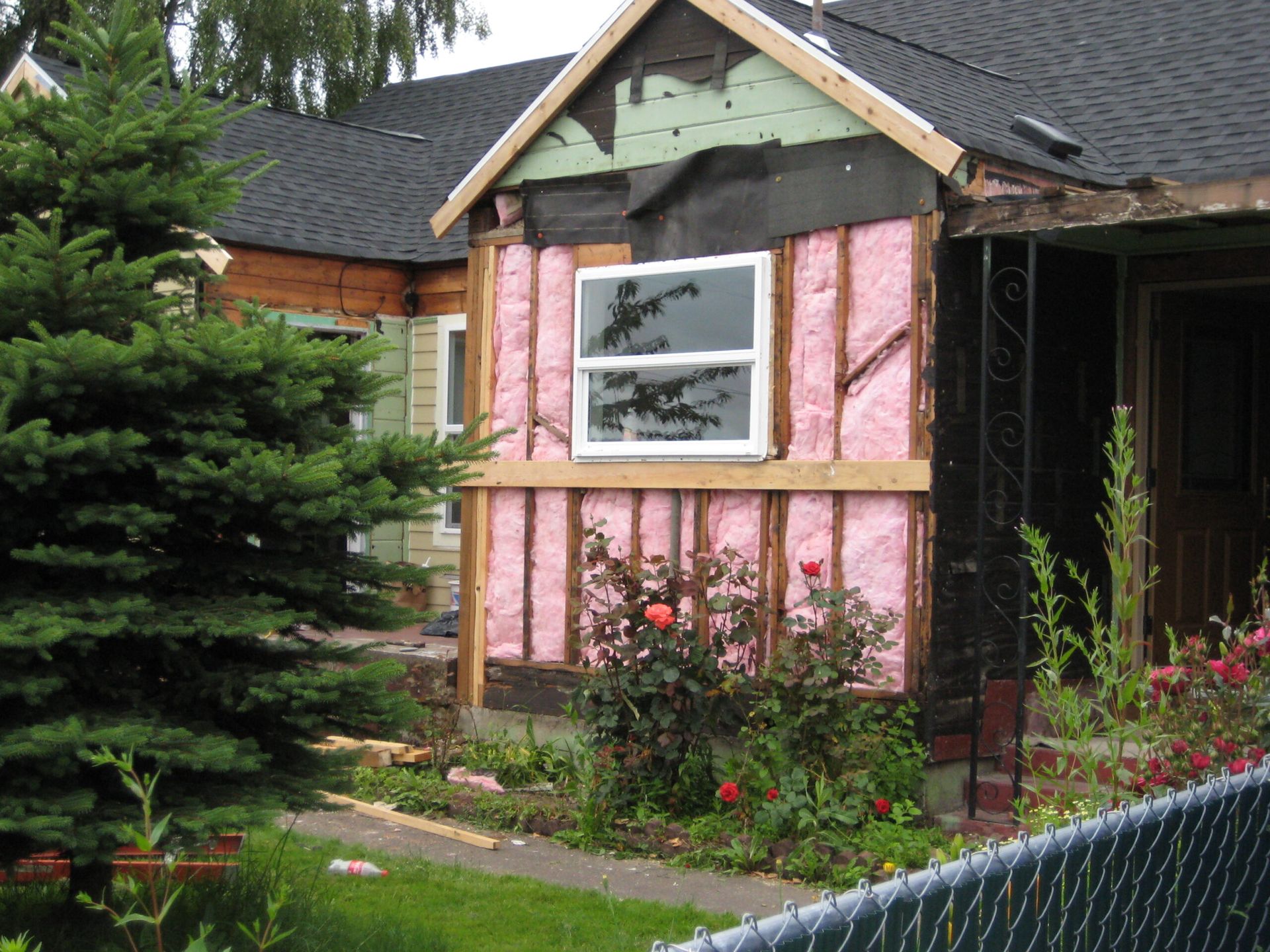 House exterior under renovation with pink insulation, a window, and a garden in front