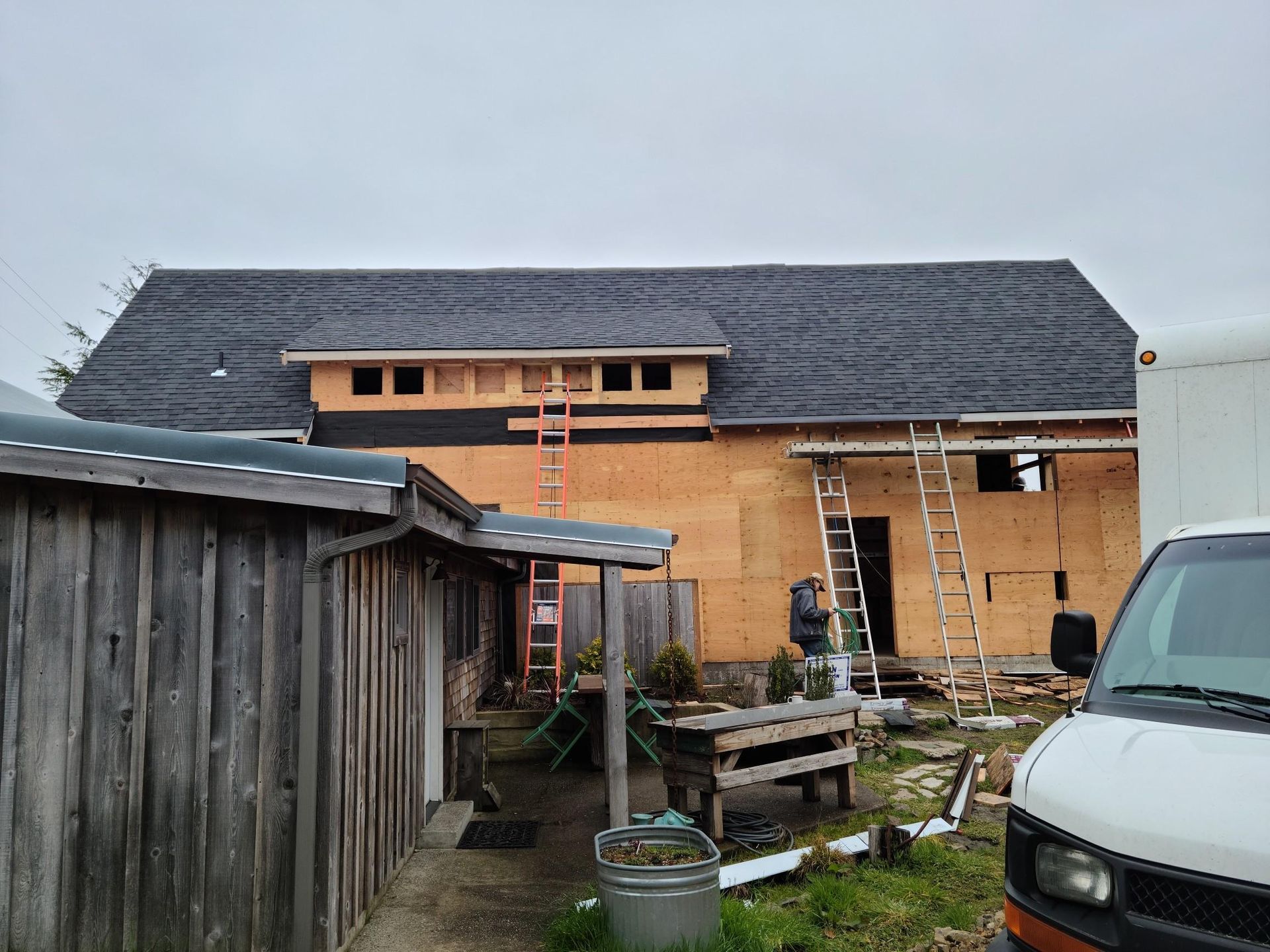 Partially built tan house with gray roof, wooden fence, and parked van in a yard