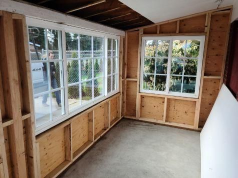 Unfinished room with exposed wall studs, carpet, and large windows letting in daylight.