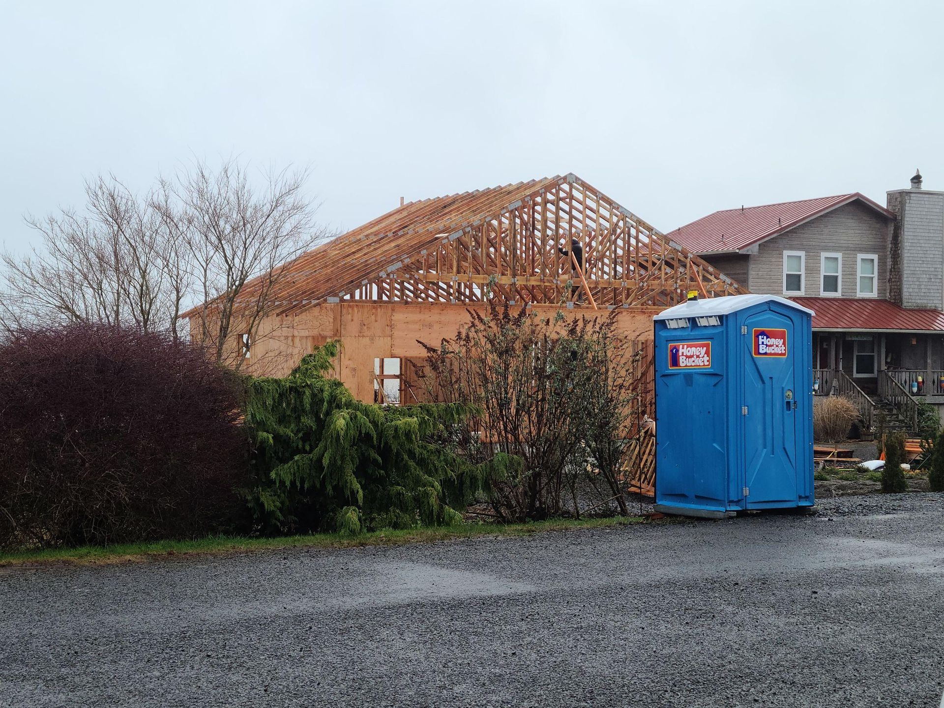 Blue portable toilet in front of a house under construction on a cloudy day