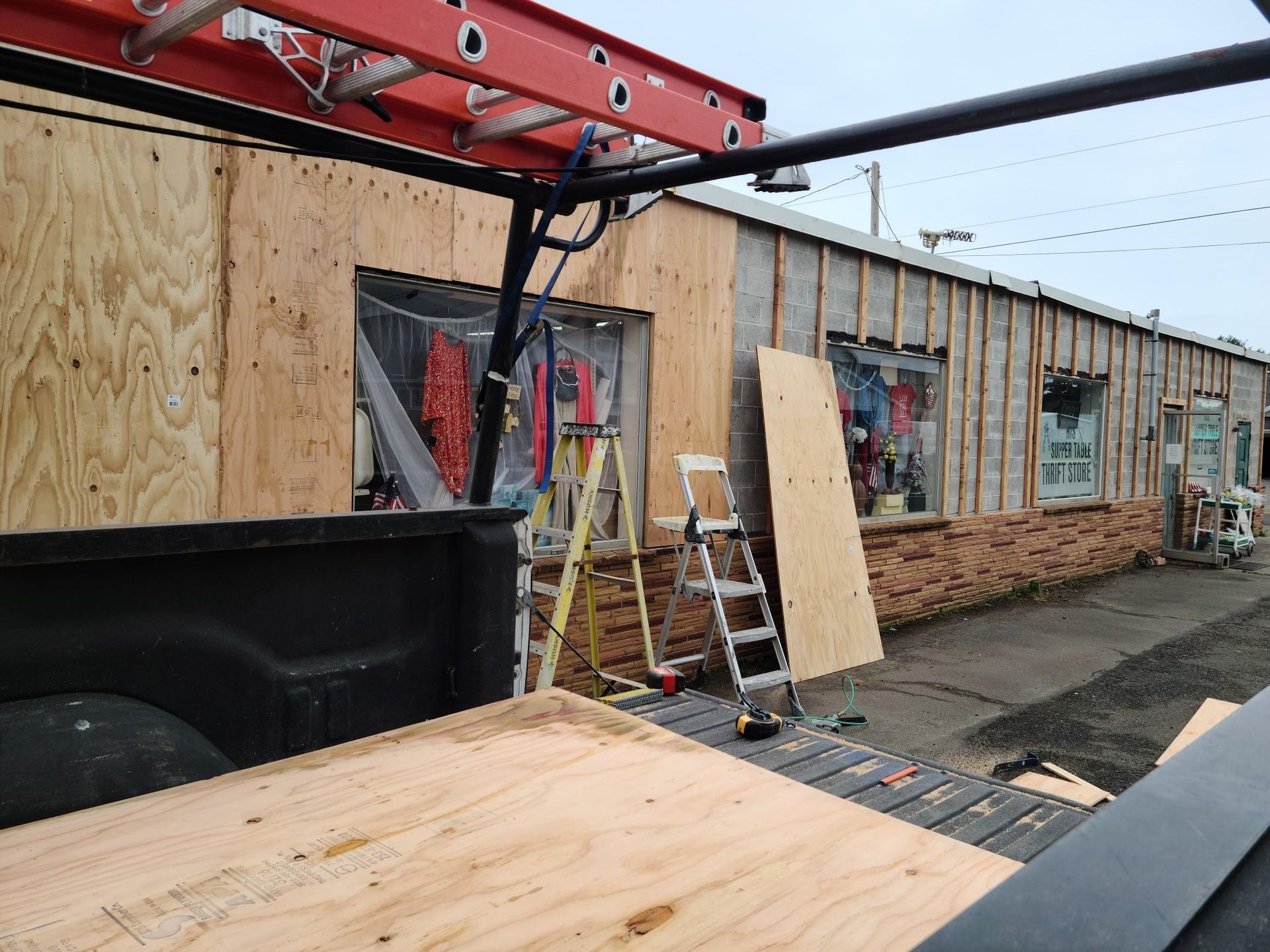 Construction site with plywood-covered building walls, ladder, and red lifting equipment overhead