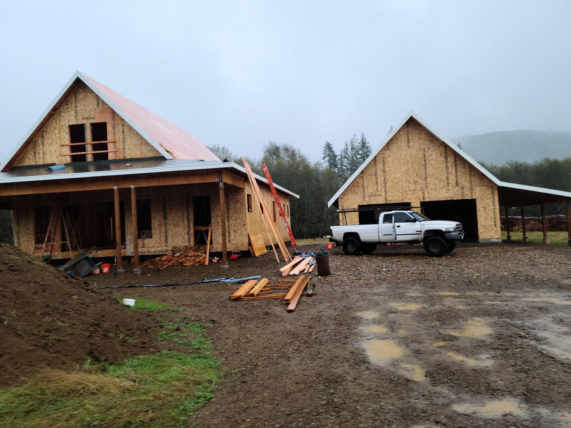 Rural construction site with two unfinished wooden houses and a white pickup truck on muddy ground