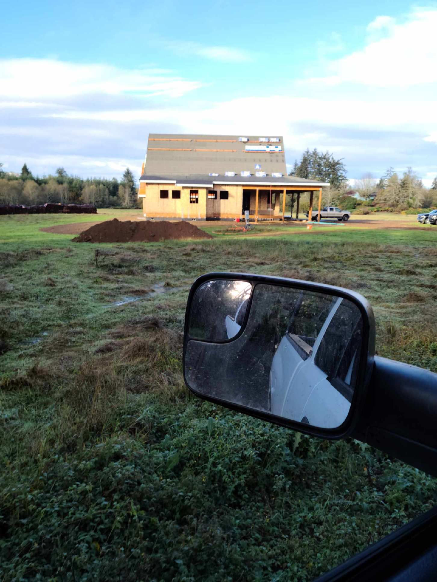 Partially built house in a field, viewed from a car side mirror in the foreground