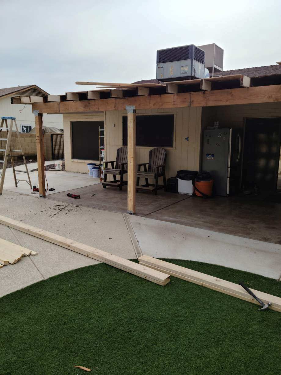 Backyard patio with chairs, cooler, and HVAC unit beside a house, with artificial turf in the foreground