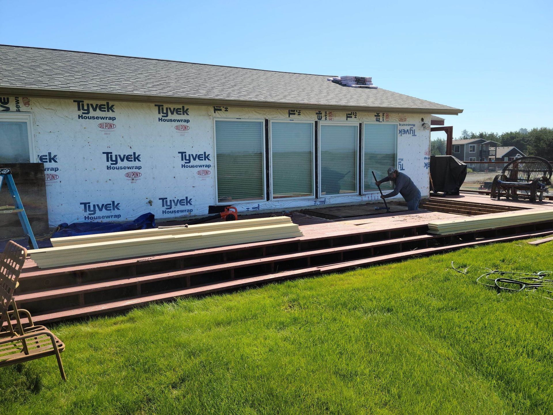 Backyard deck under construction beside a house with Tyvek wrap and sliding glass doors
