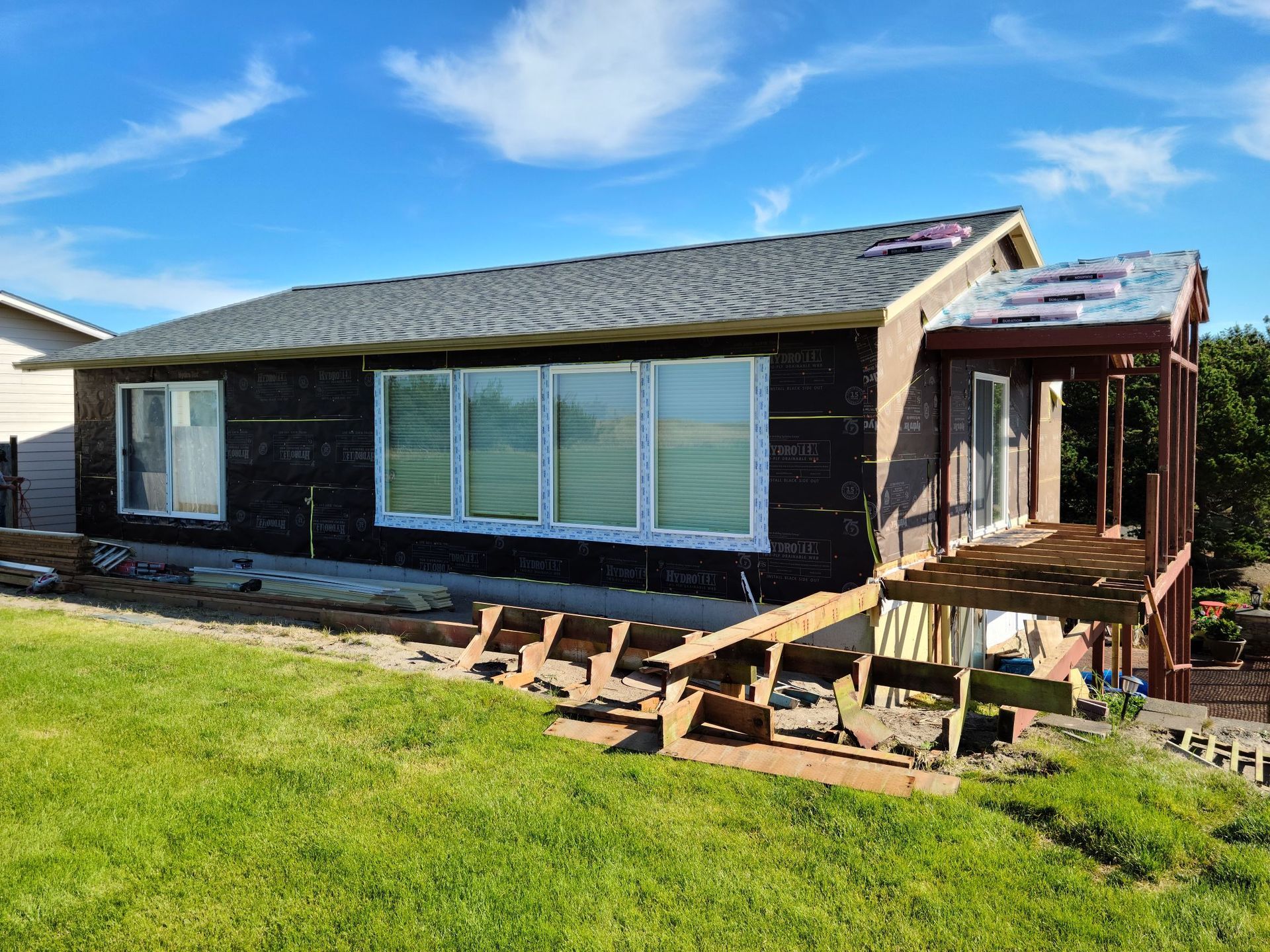 Single-story house with dark siding, damaged deck, and skewed steps in a sunny yard