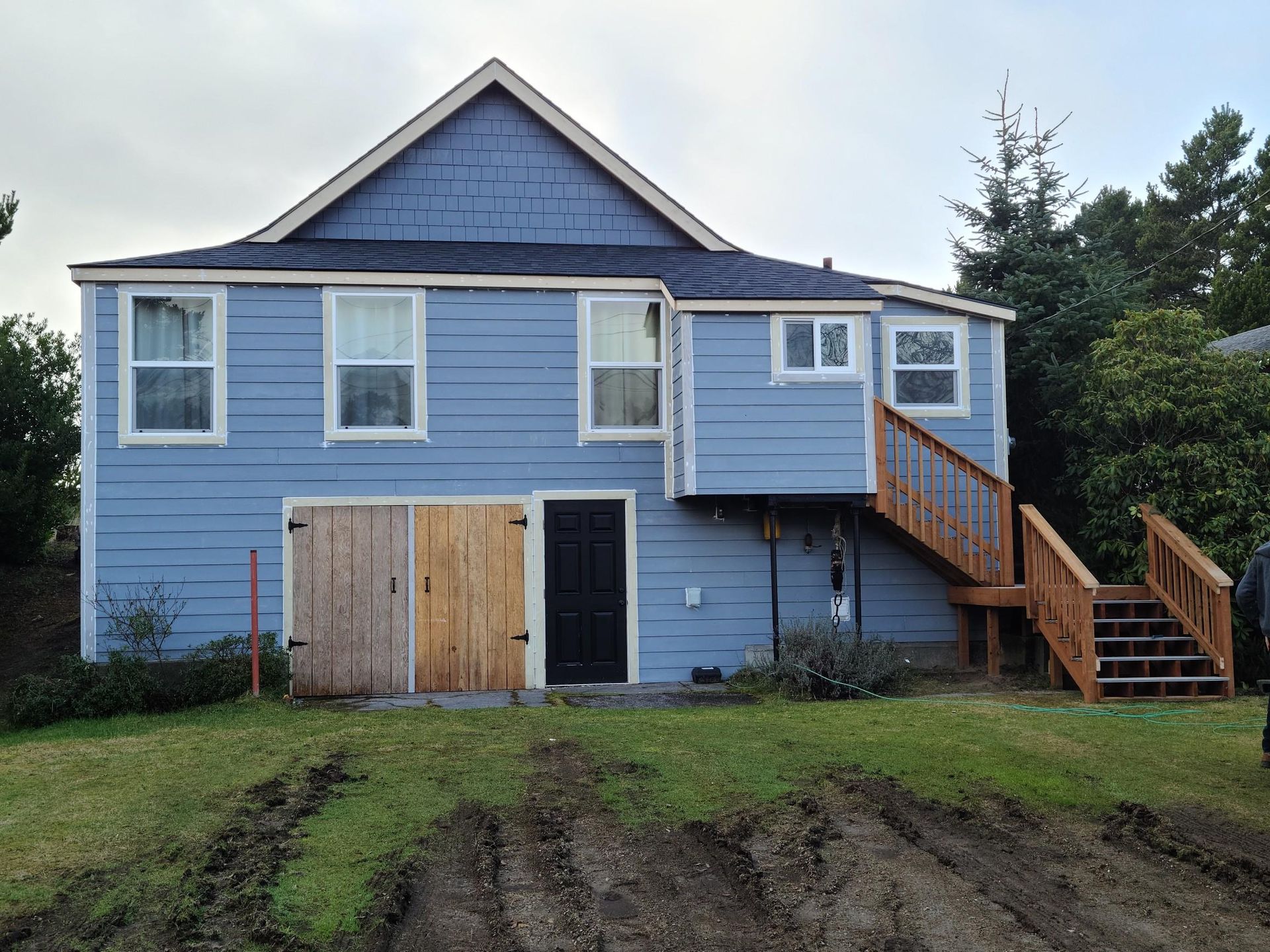Blue two-story house with white trim, boarded windows, and wooden stairs on a grassy lot