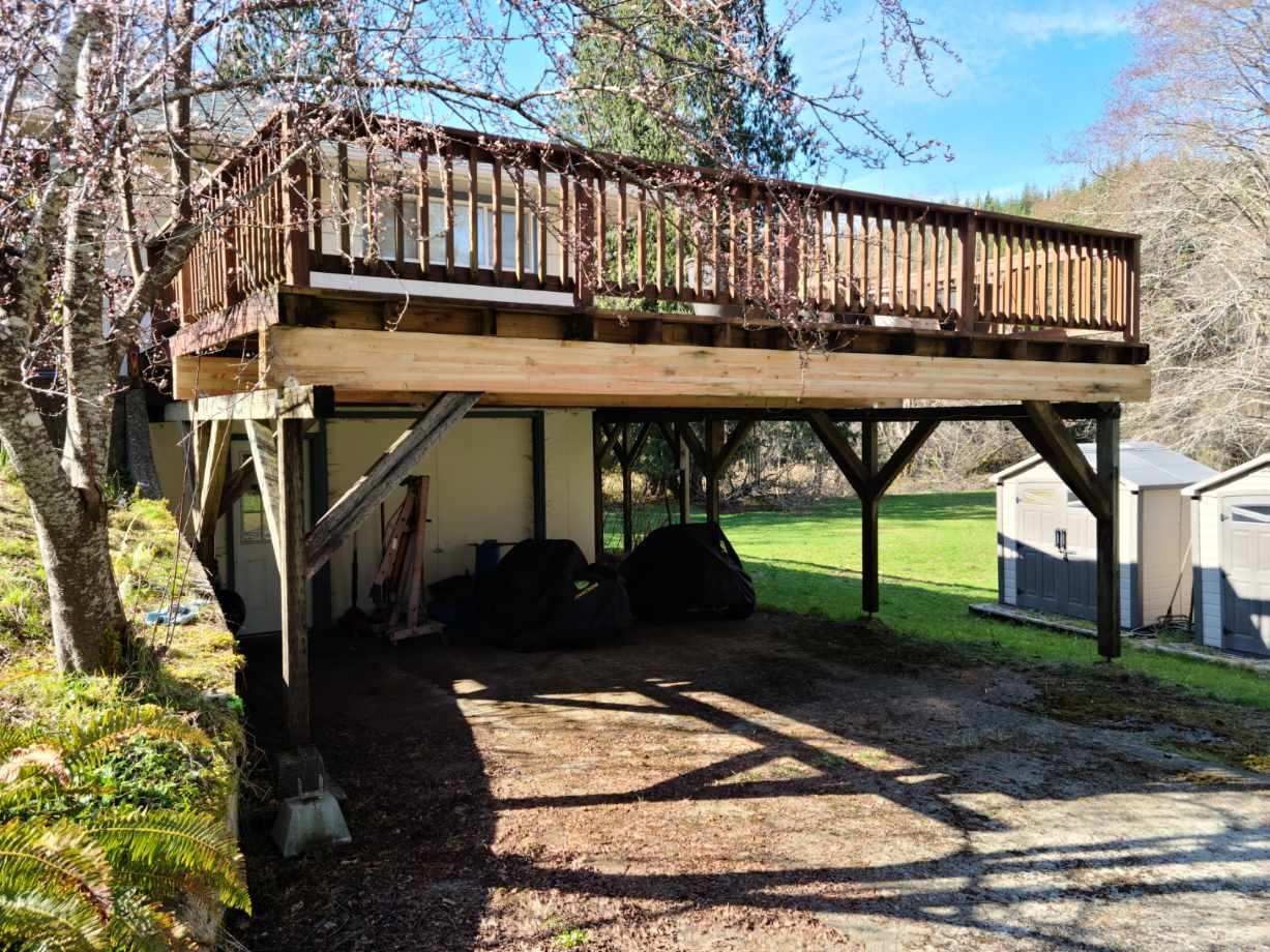 Raised wooden deck over a gravel driveway beside a house, with support posts and a ladder underneath.