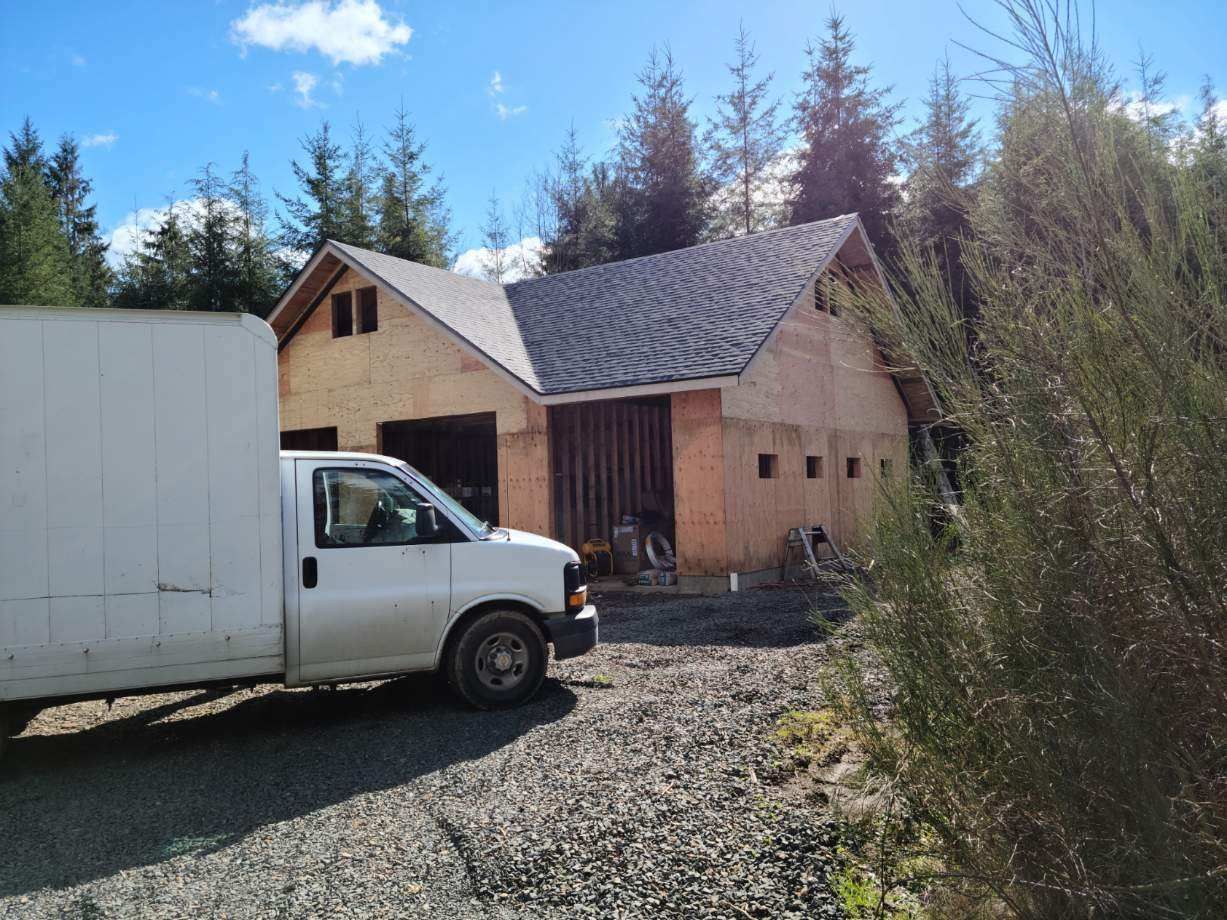 White truck parked by a small house under construction beside a gravel driveway and tall trees