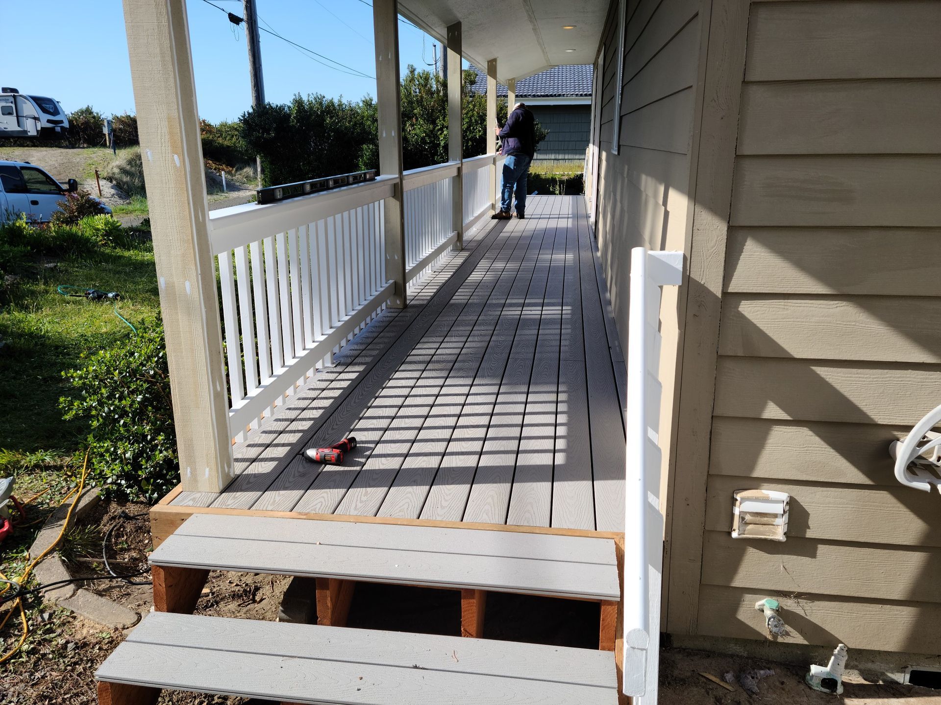 Covered porch with white railing, wooden steps, and a person standing at the far end.