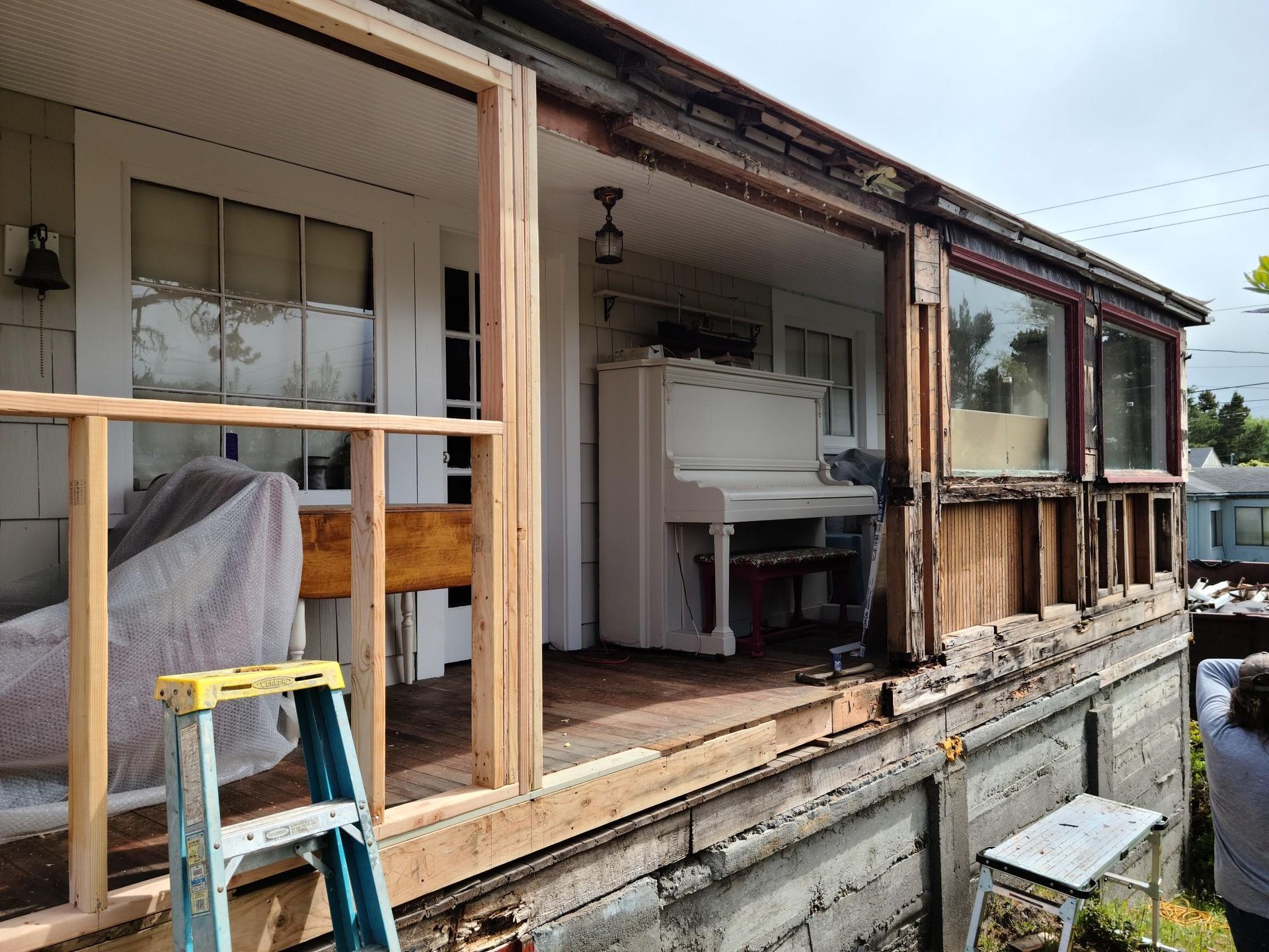 Partially renovated porch with exposed framing, piano, and step ladder beside a house