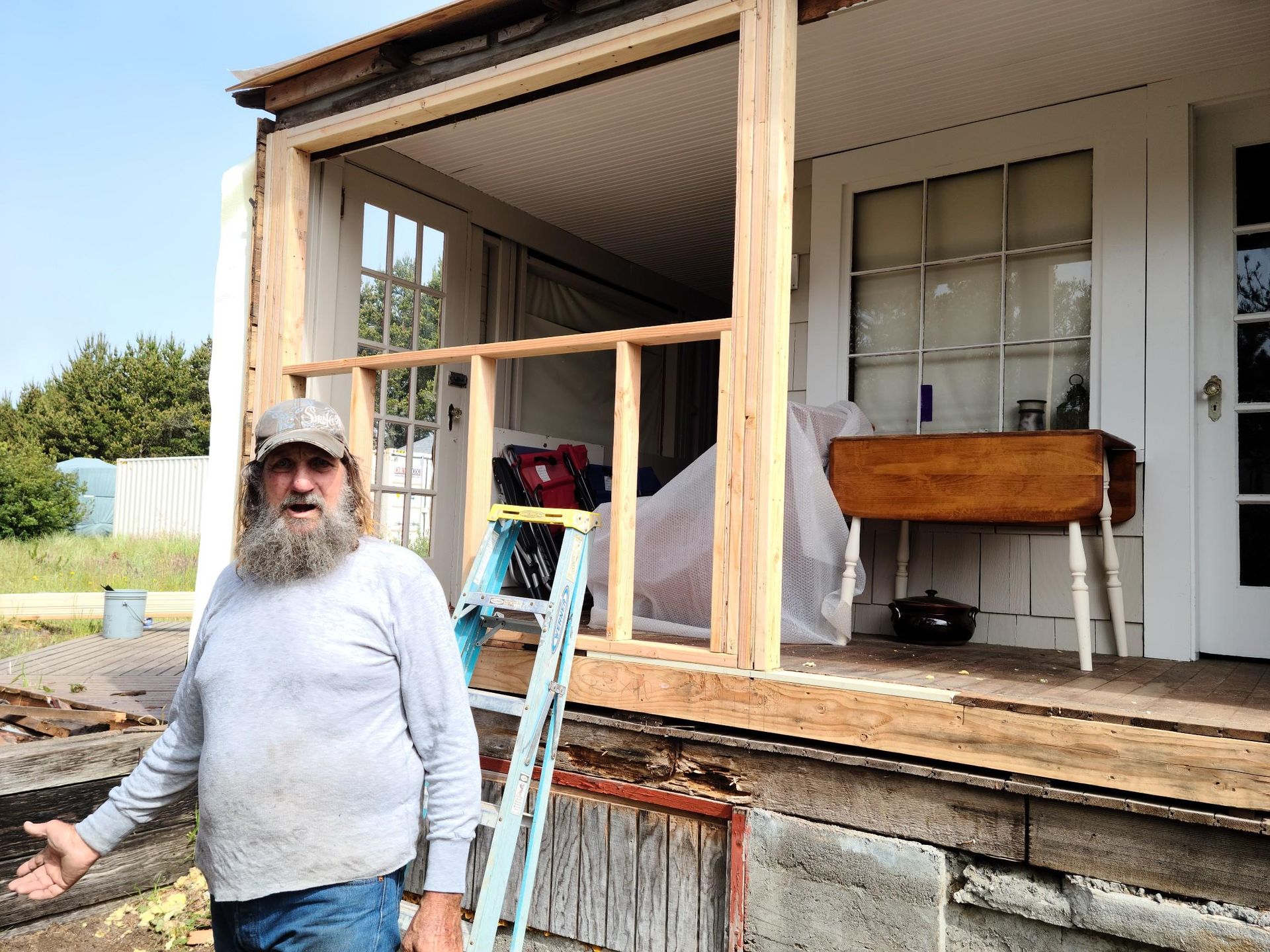Man standing on a porch beside a ladder and wooden railing under construction