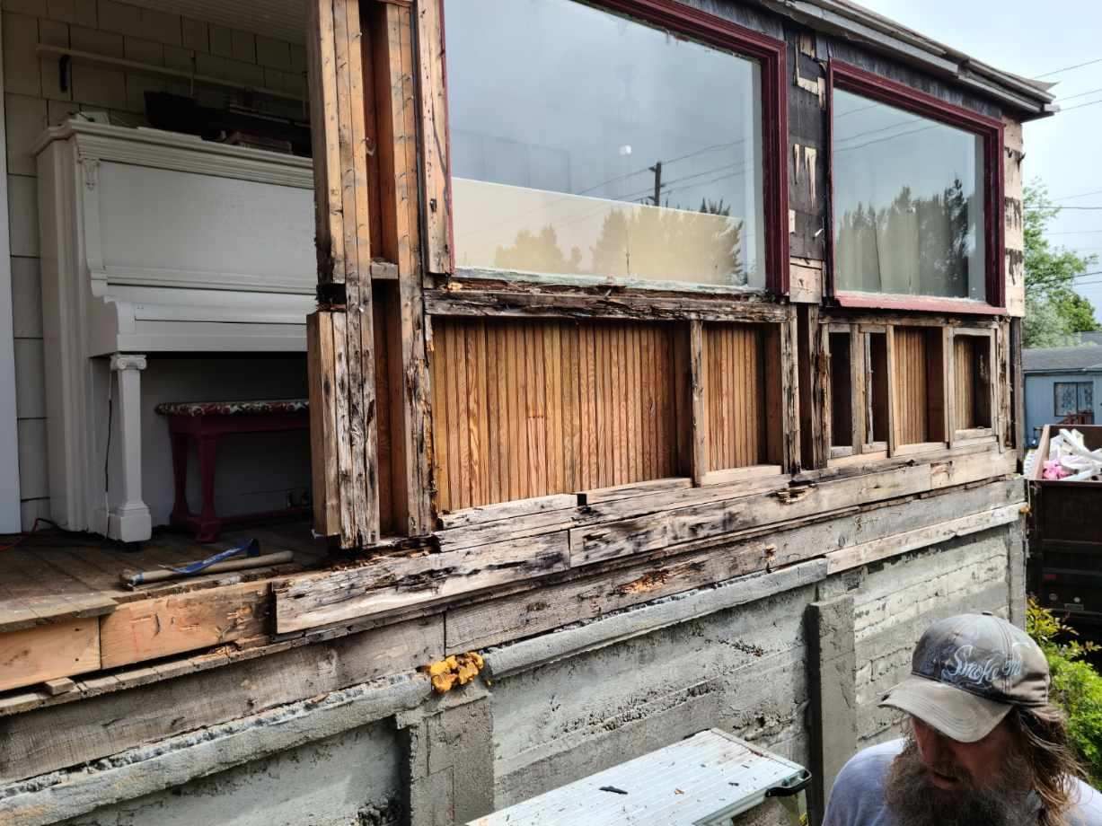 Renovating a weathered house exterior with exposed wood framing and broken windows