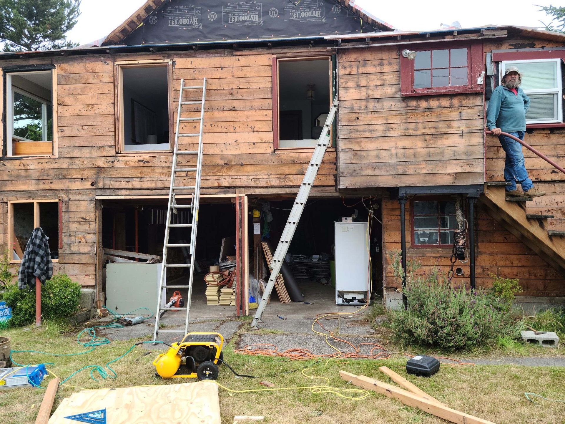 Partially renovated two-story house with ladders, open windows, and a worker on the right-side stairs