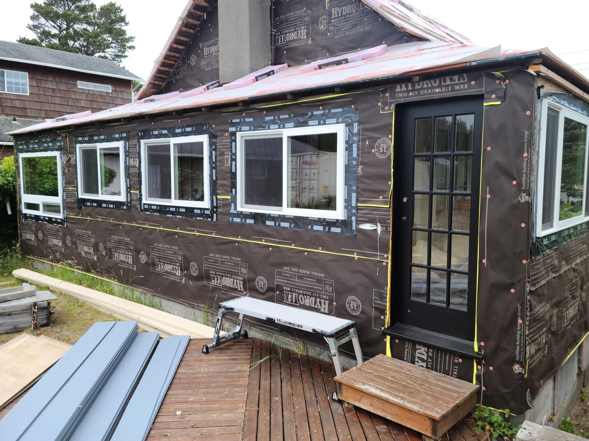 Exterior of a house under construction with dark siding, white-trimmed windows, and a black door