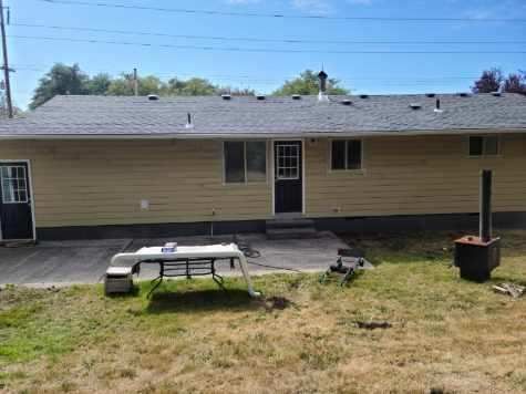 Single-story beige house with dark roof and backyard patio, picnic table, and fire pit.