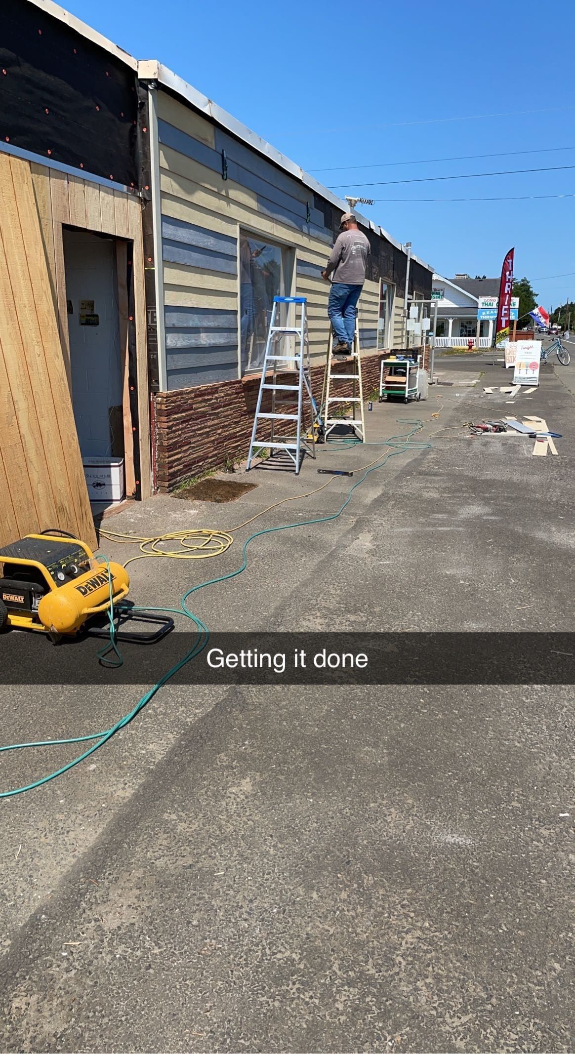 Row of storefronts with workers on ladders, tools on the ground, and a sunny blue sky overhead