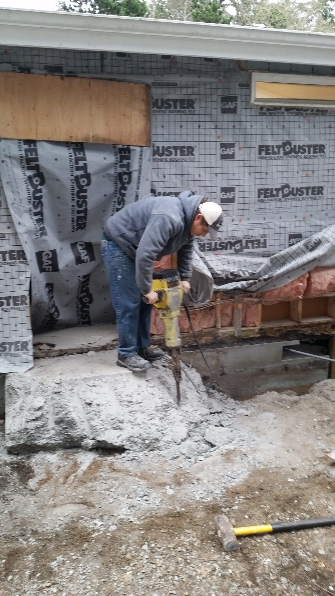 Worker using a jackhammer on a concrete floor at a construction site with brick walls and insulation boards