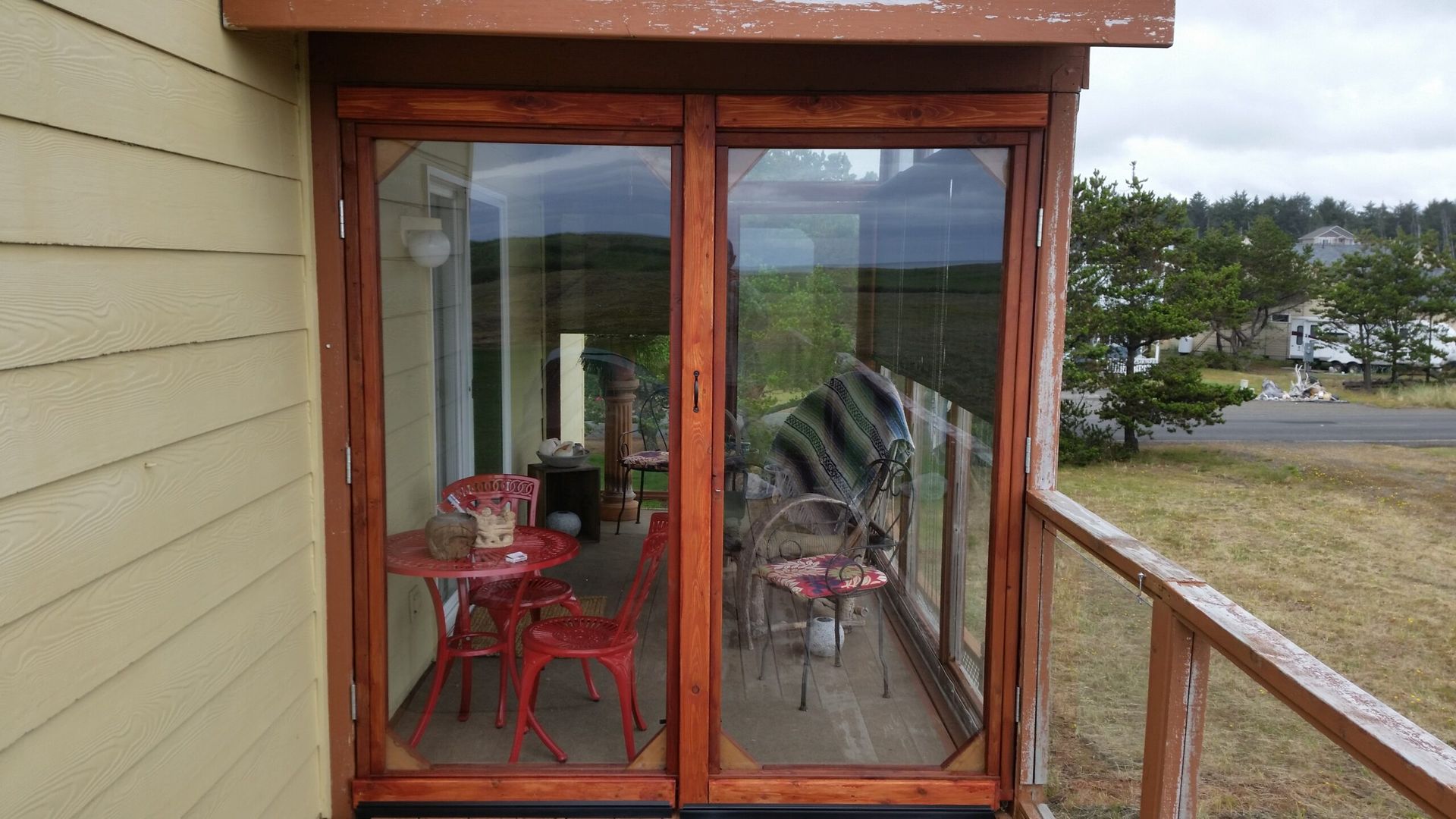 Red bistro chairs on a small glassed-in balcony overlooking a grassy landscape and road