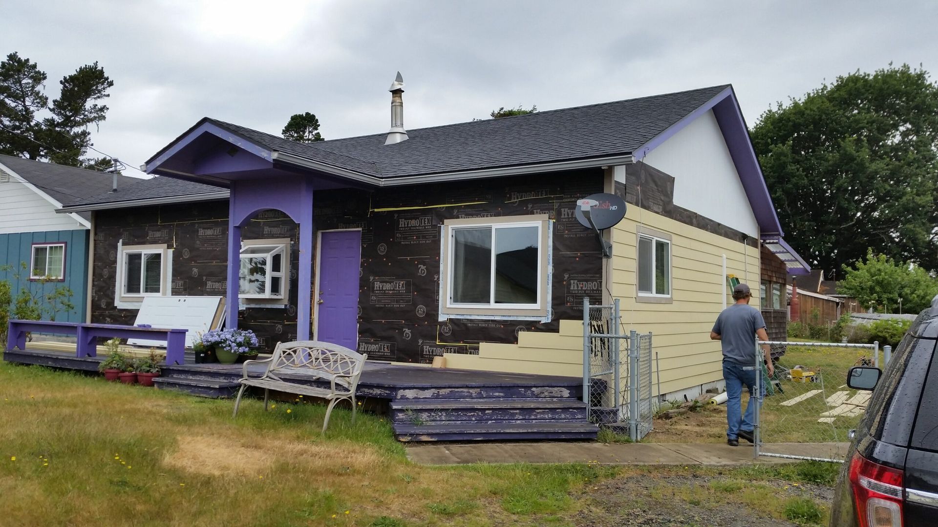 Purple and beige house with a bench and a person standing in the yard