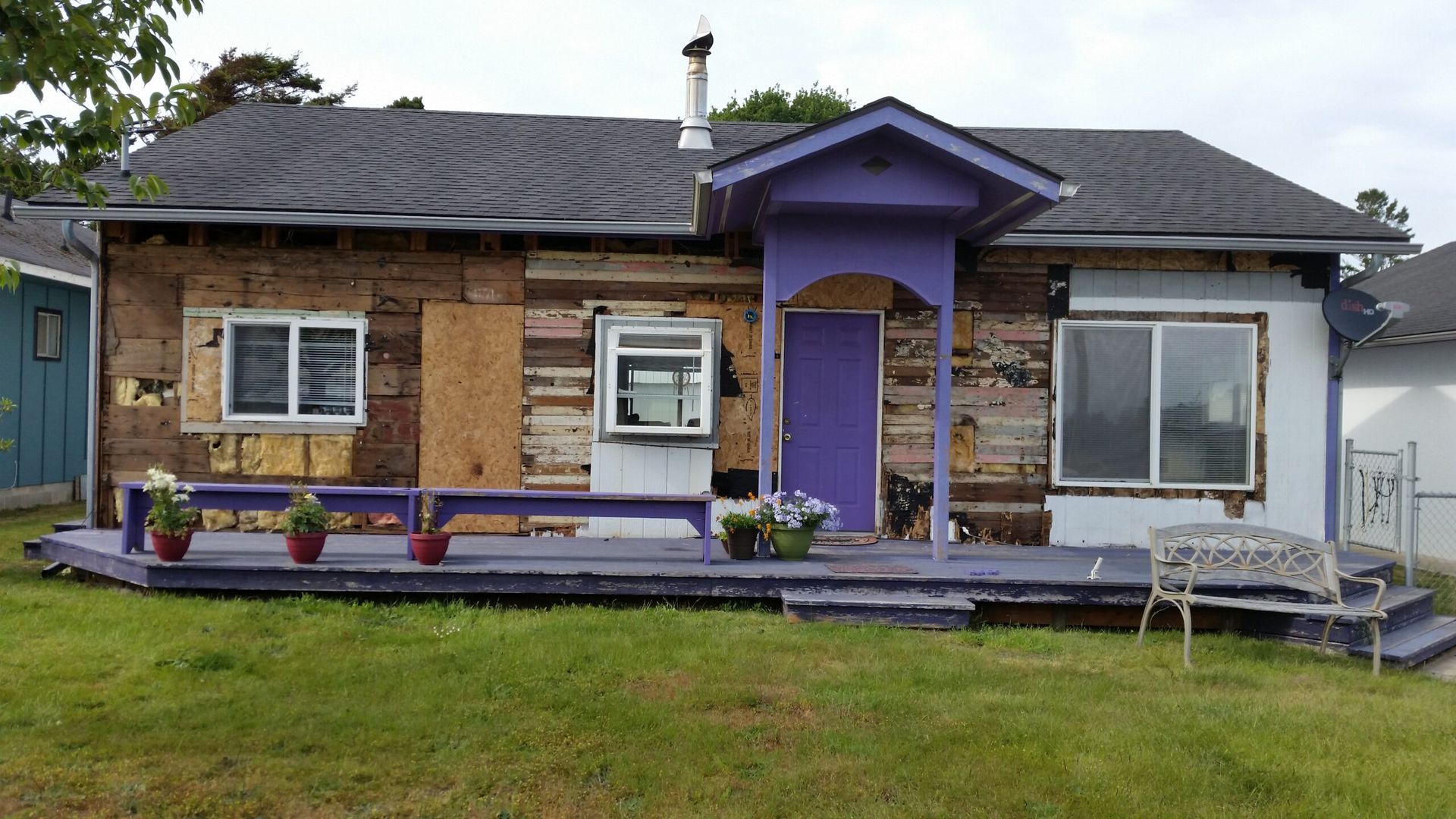 Single-story house with purple trim and front porch, gray roof, and green lawn.