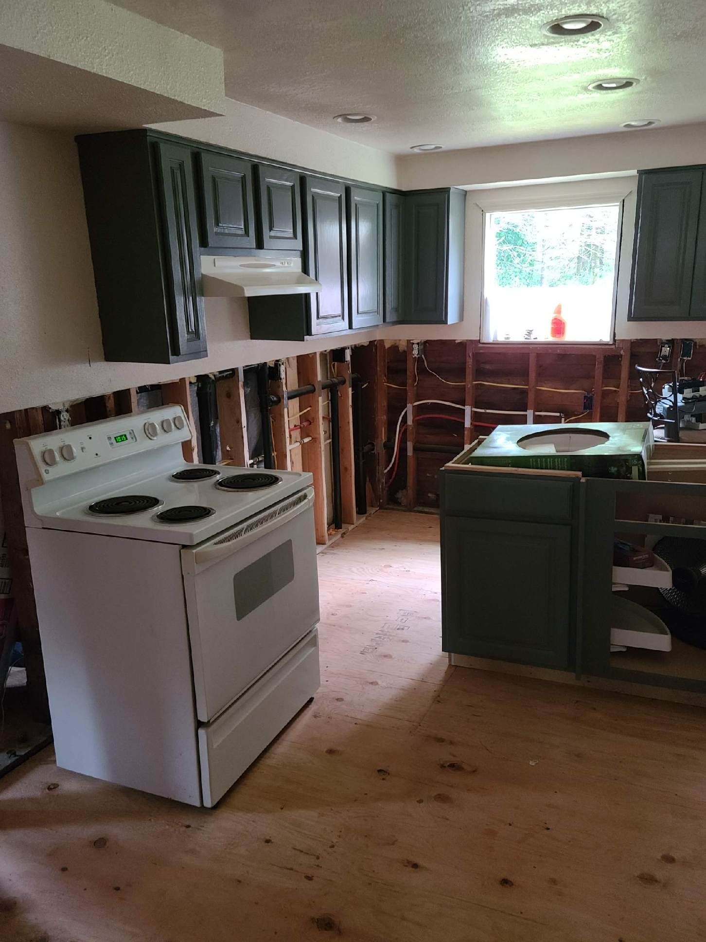 Partially renovated kitchen with dark cabinets, white stove, and exposed walls around the sink area