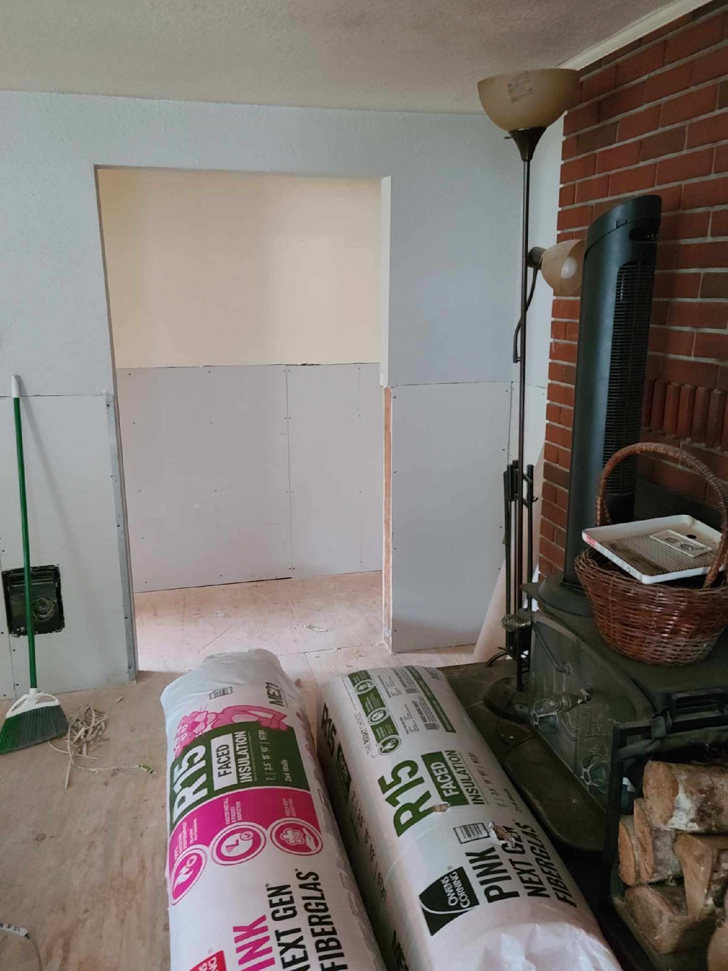 Room under renovation with drywall in doorway, paint and supplies on floor, fireplace and lamp at right