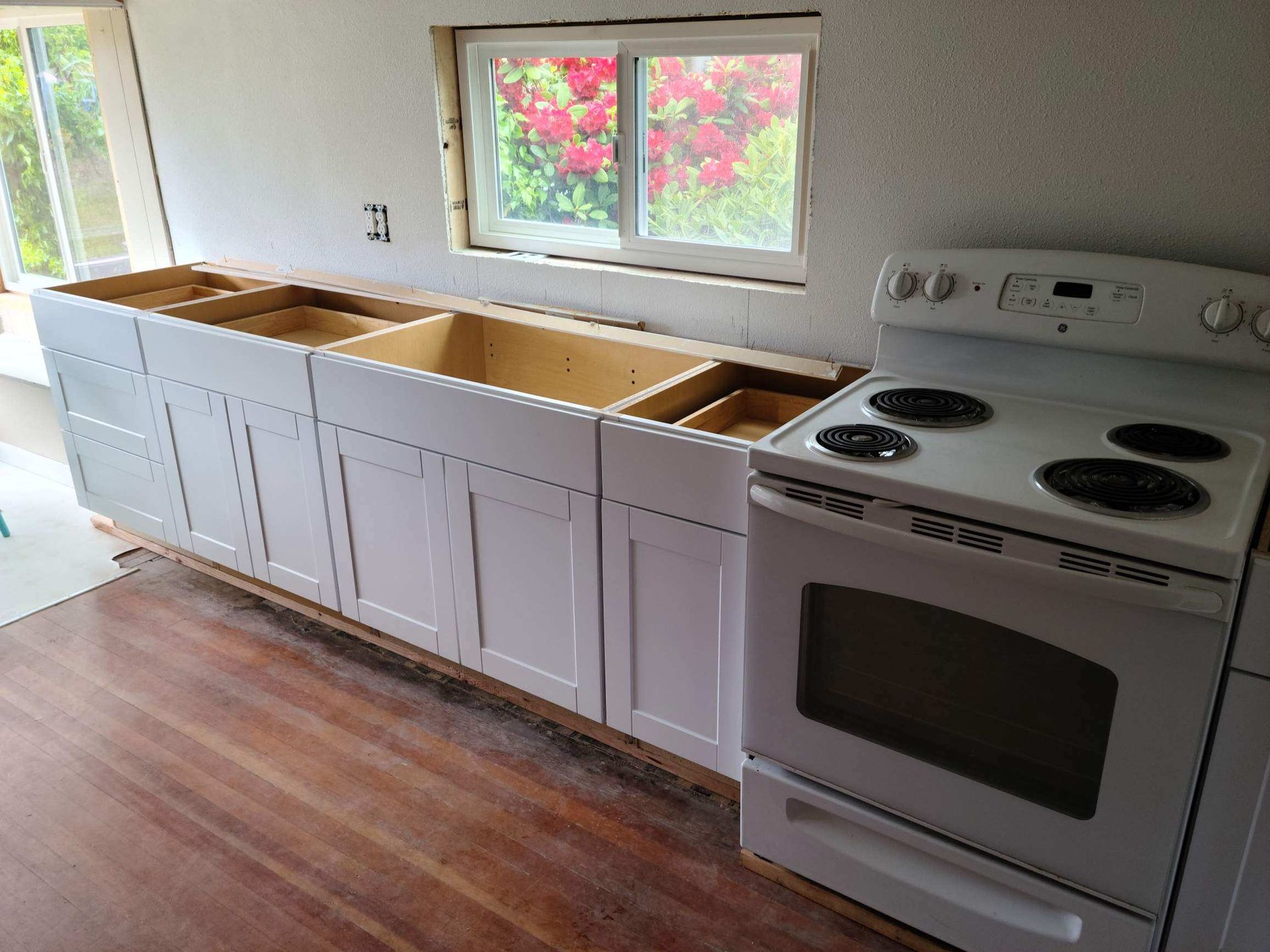 Kitchen with white cabinets, unfinished countertops, window, and a white stove beside wood flooring
